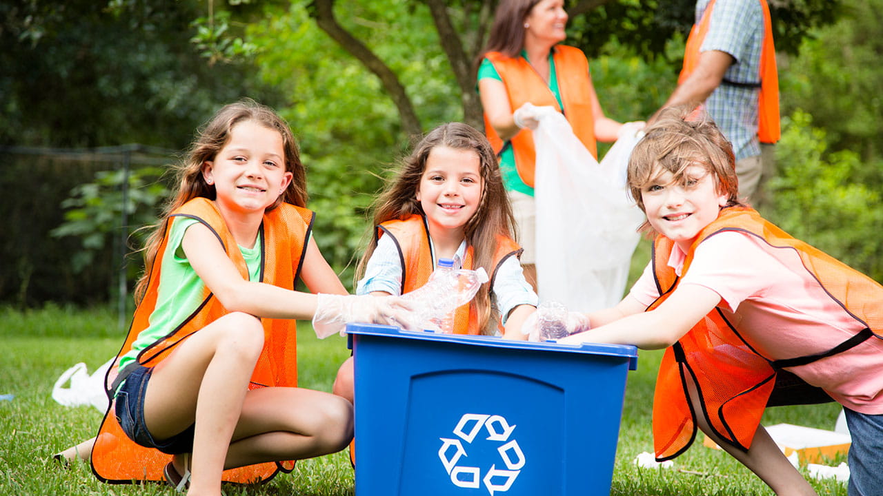 A family shown picking up trash and putting recyclables into a bin